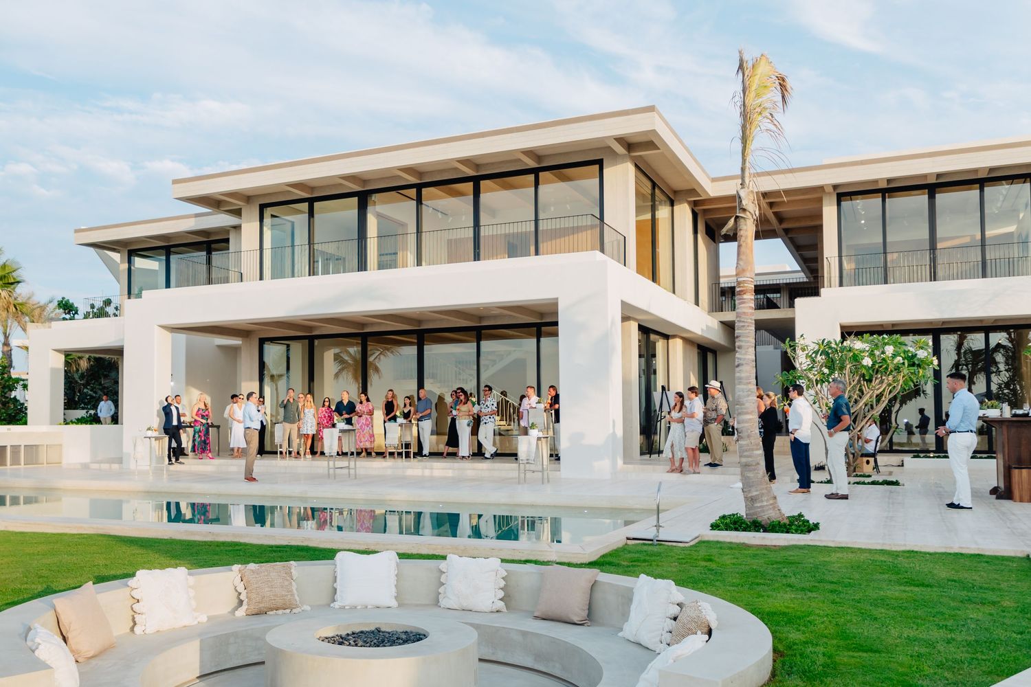Modern luxury villa with glass walls and outdoor seating areas overlooking a scenic landscape at sunset.