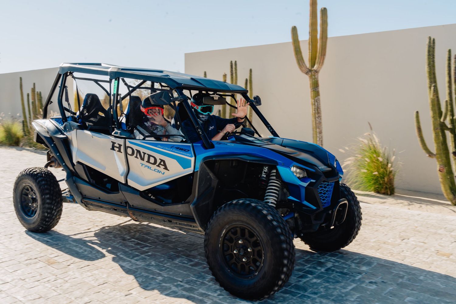 Blue off-road dune buggy racing through desert terrain with saguaro cacti in the background.