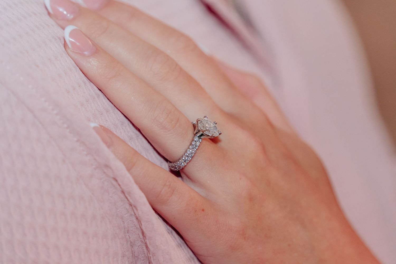Close-up of an engagement ring on a person's finger against a pink fabric background.
