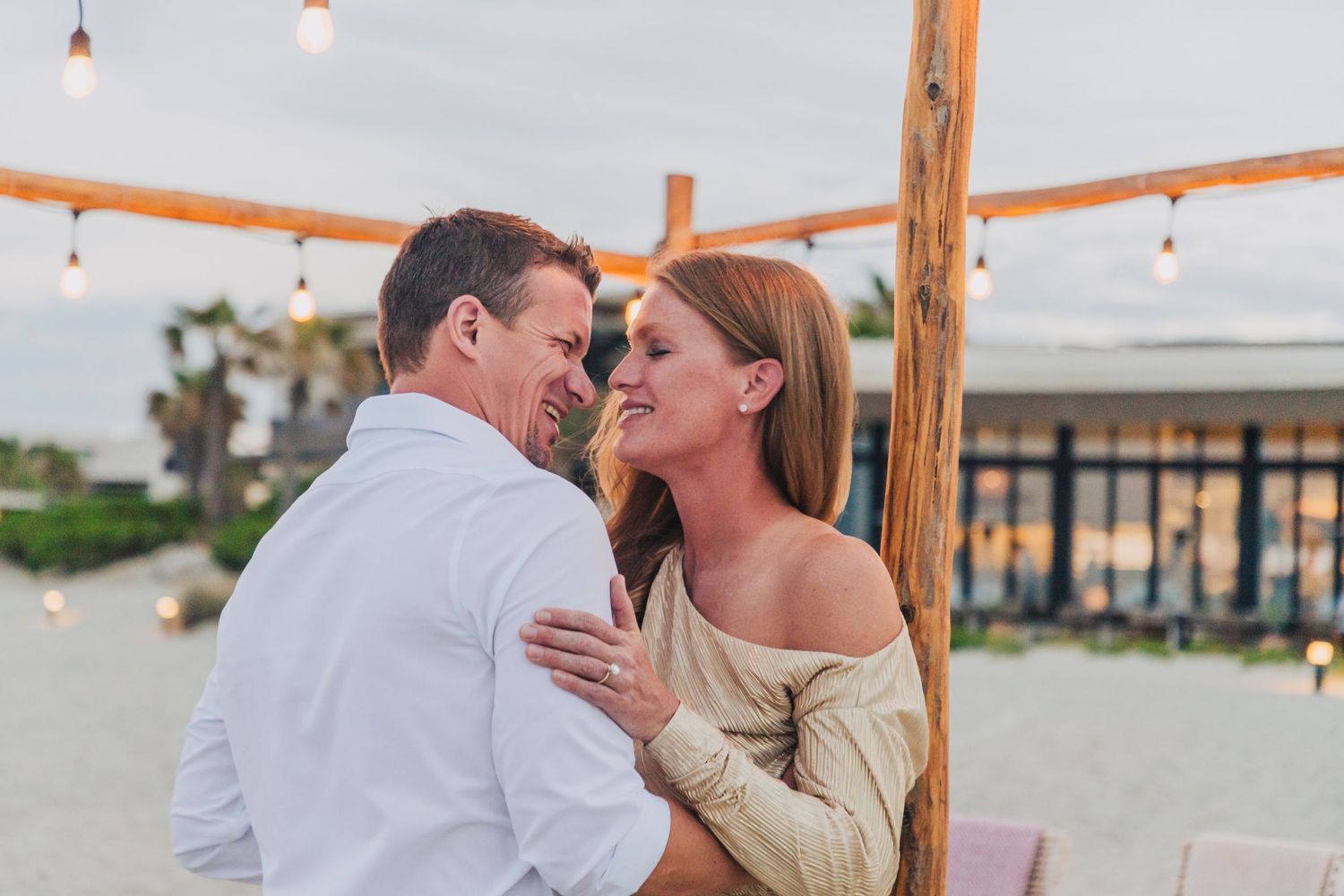 Sweet celebration moment under wooden arch with beach backdrop.