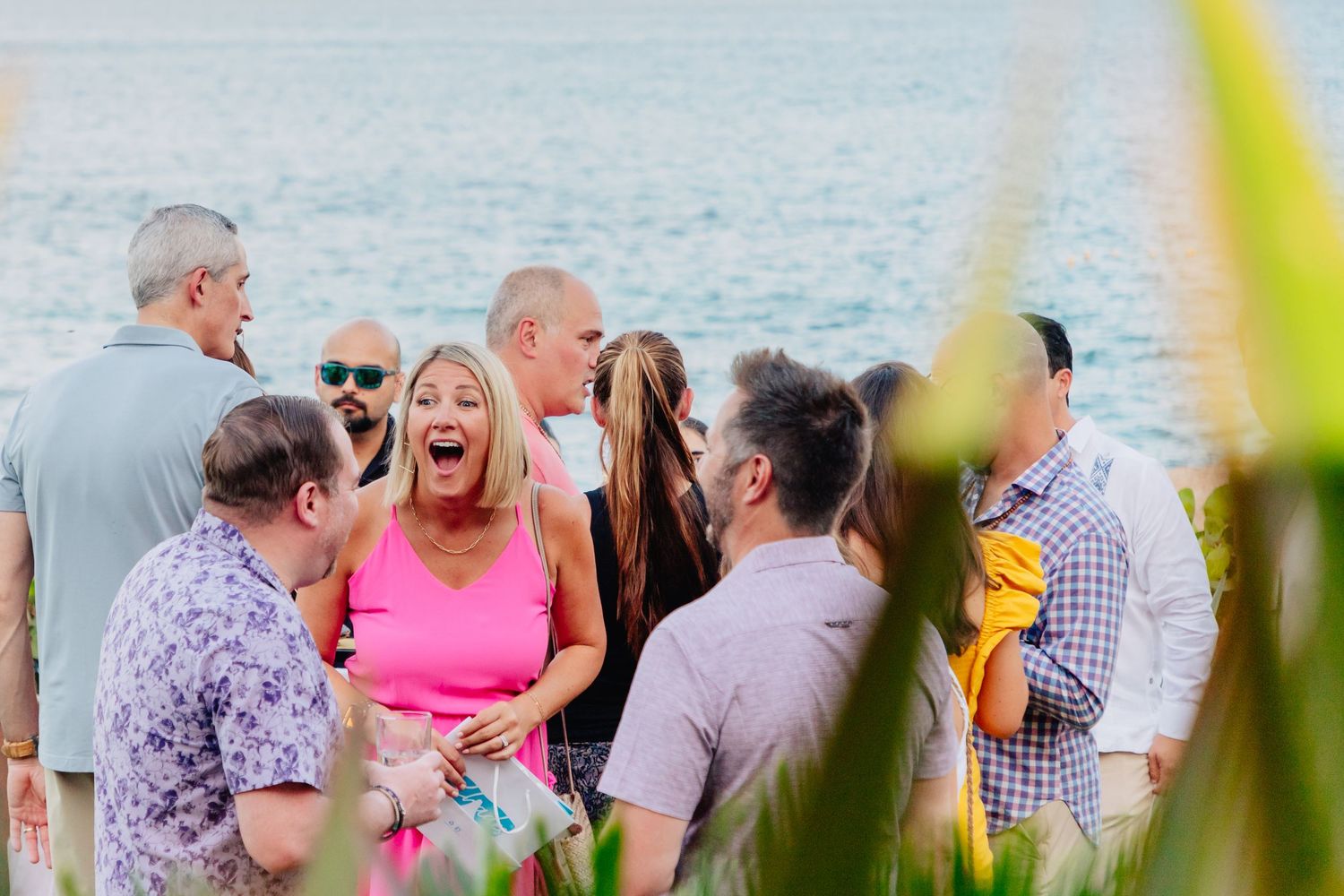 Group of people gathered outdoors at a beach event with pink and purple attire visible through beach grass.