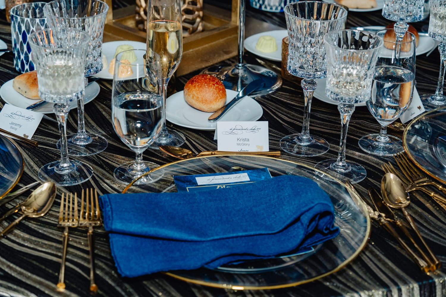 Formal place settings with crystal glassware and blue napkins on mirrored charger plates.