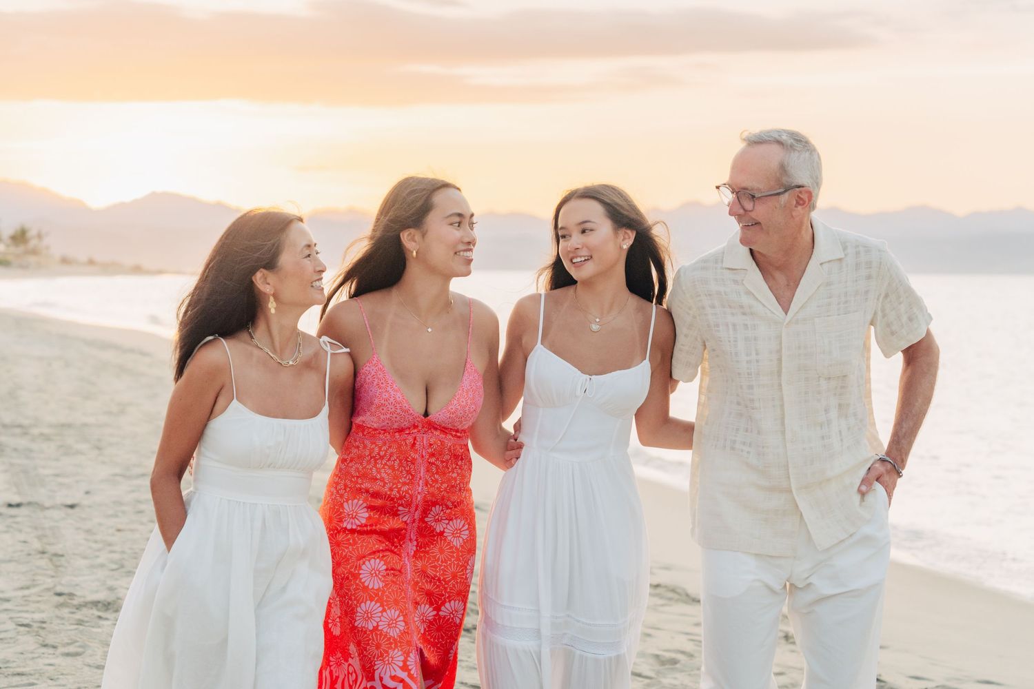 A group in white and coral outfits walking along a sandy beach during sunset in Hawaii.