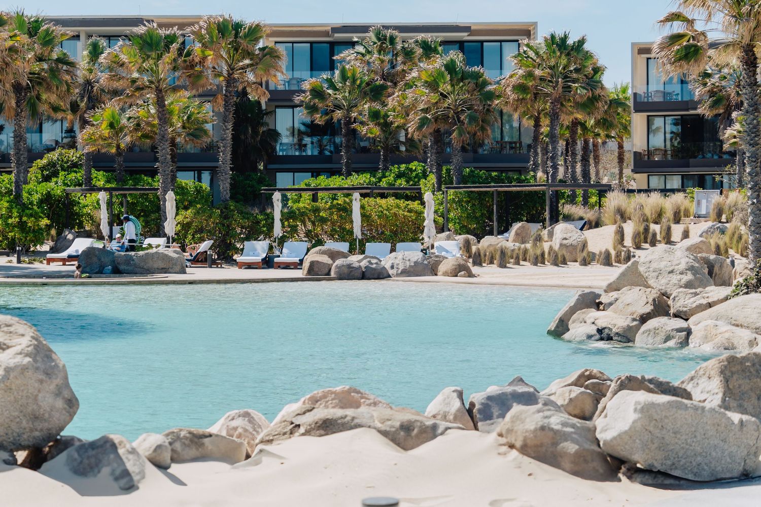 Luxury beachfront resort with palm trees and turquoise water surrounding a rocky shoreline.