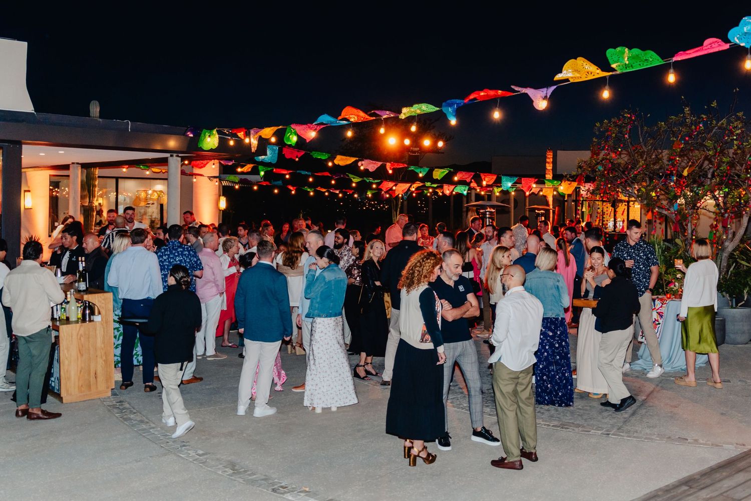 Colorful string lights illuminate an outdoor evening party with dancing guests.