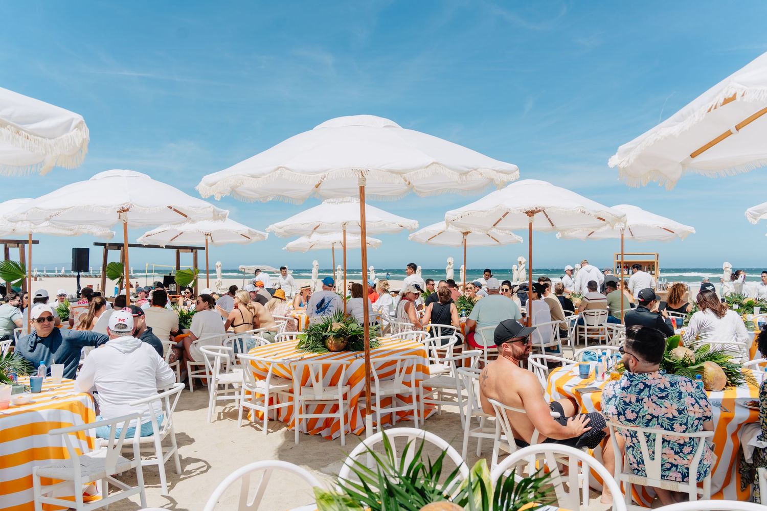 White beach umbrellas and lounge chairs line a pristine sandy shoreline under bright blue skies.