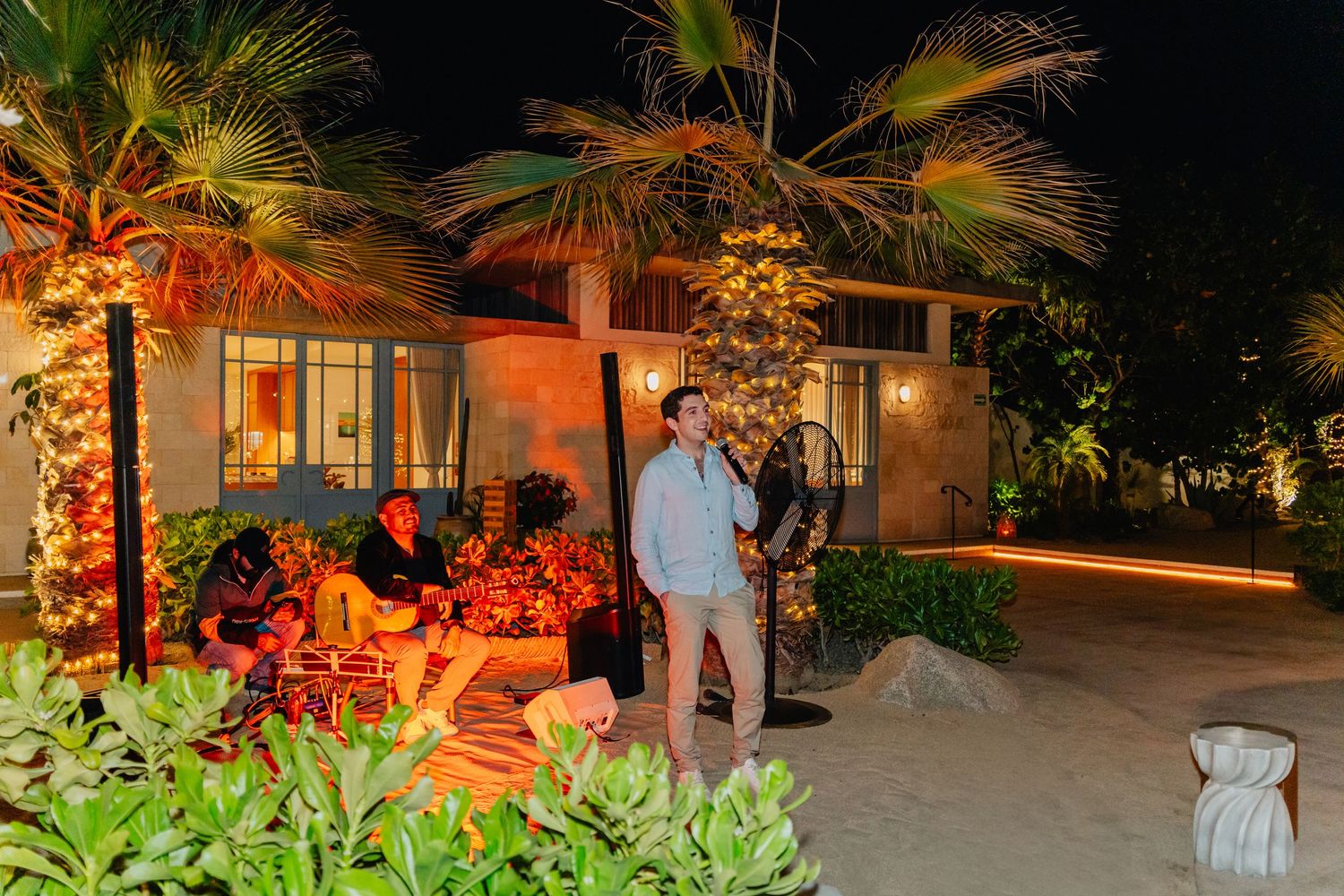 Illuminated outdoor patio area at night with tropical plants and warm lighting creating an inviting ambiance.