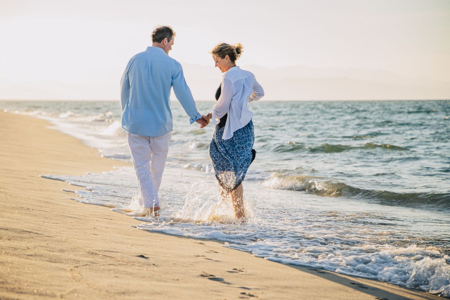 Couple strolling along a scenic beach shoreline at sunset with waves gently rolling in.