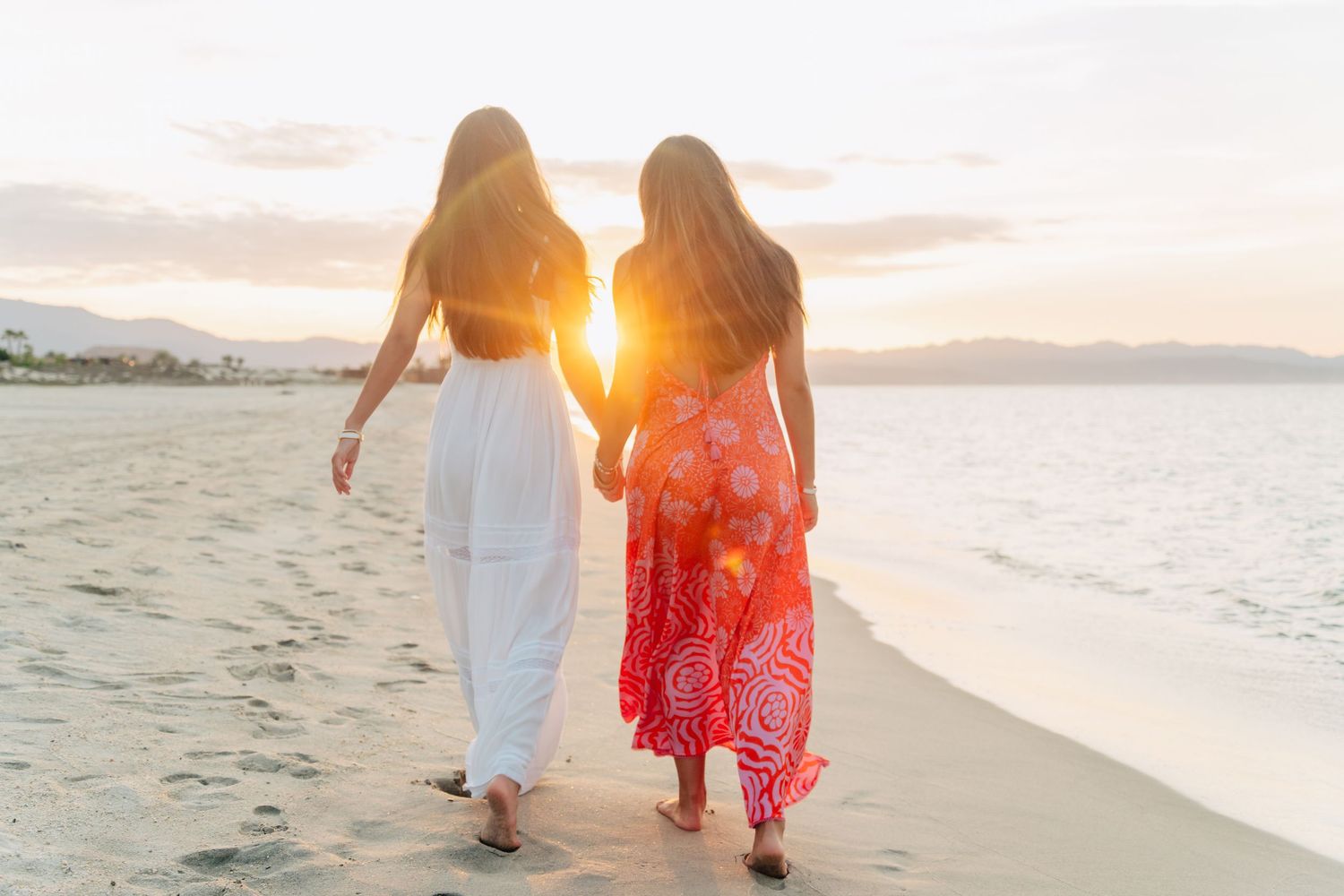 People strolling along a beach at golden hour with mountains in the distance.