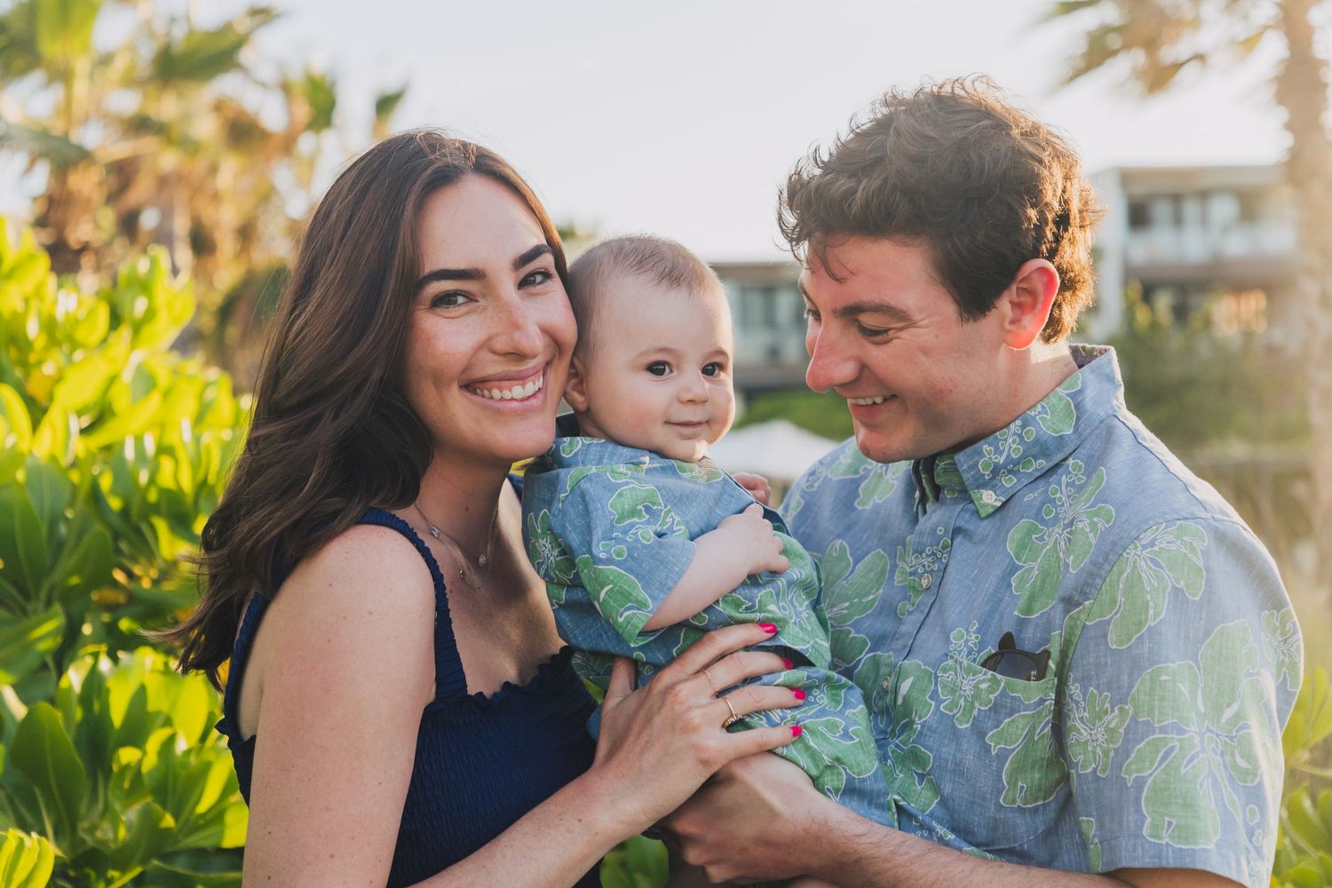 Family in coordinating outfits sharing joyful moments together in a sun-drenched garden setting with palm trees.