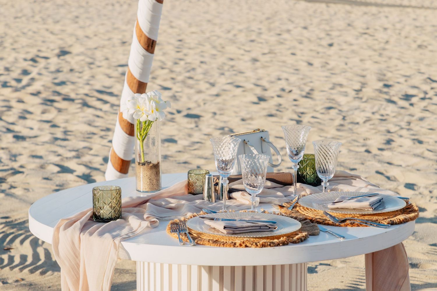 Elegant beach dining setup with white tablecloth and natural driftwood decor.