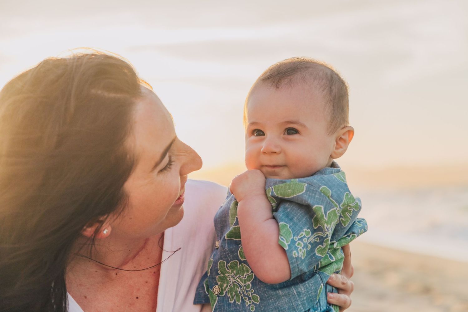 Tender moment shared between parent and baby on beach at sunset.