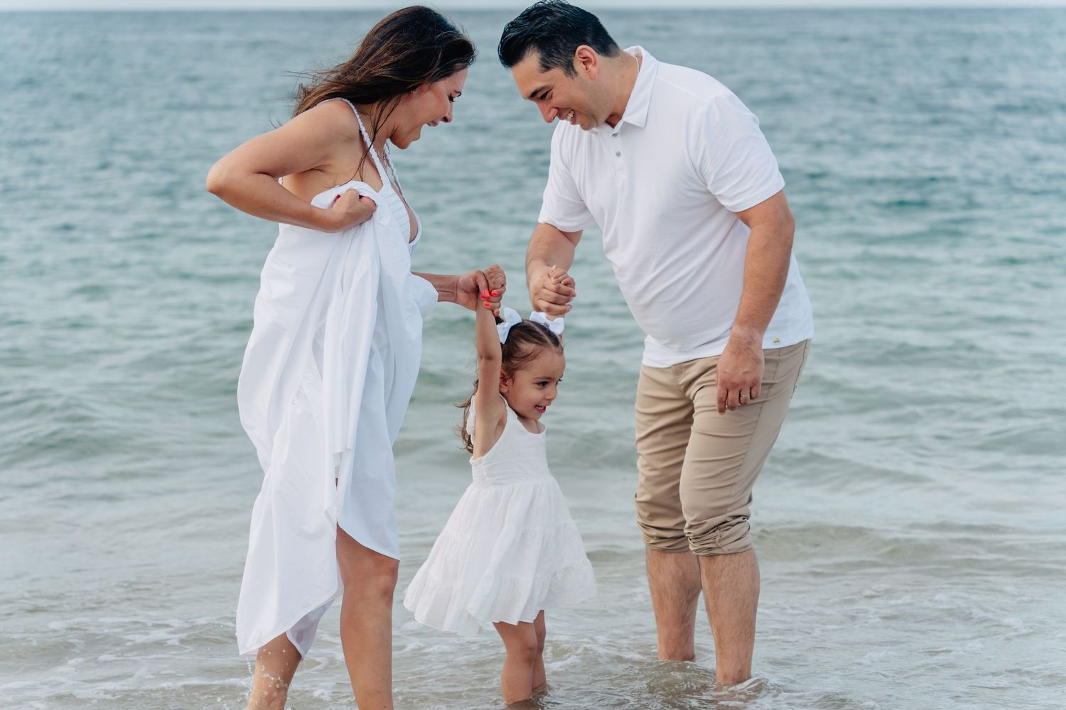 A cheerful family moment at the beach with matching white outfits as they play in the shallow water.