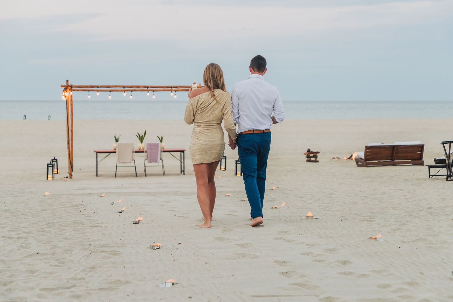 Couple walking along beach after romantic proposal setup.