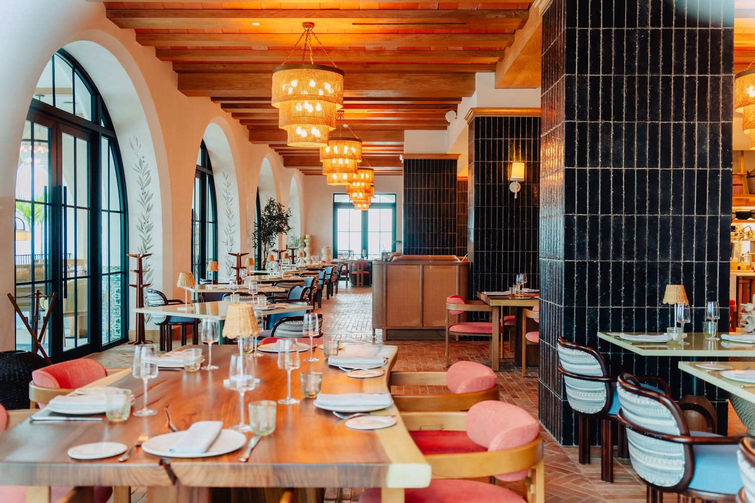 Modern hotel lounge interior with exposed wooden beams, elegant chandeliers, and plush pink seating arrangements.
