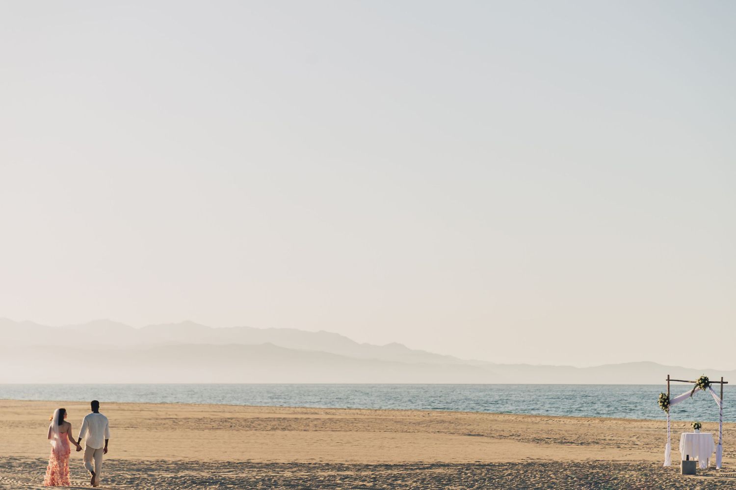 People walk along a vast desert landscape with mountains in the distance and a clear blue sky overhead.