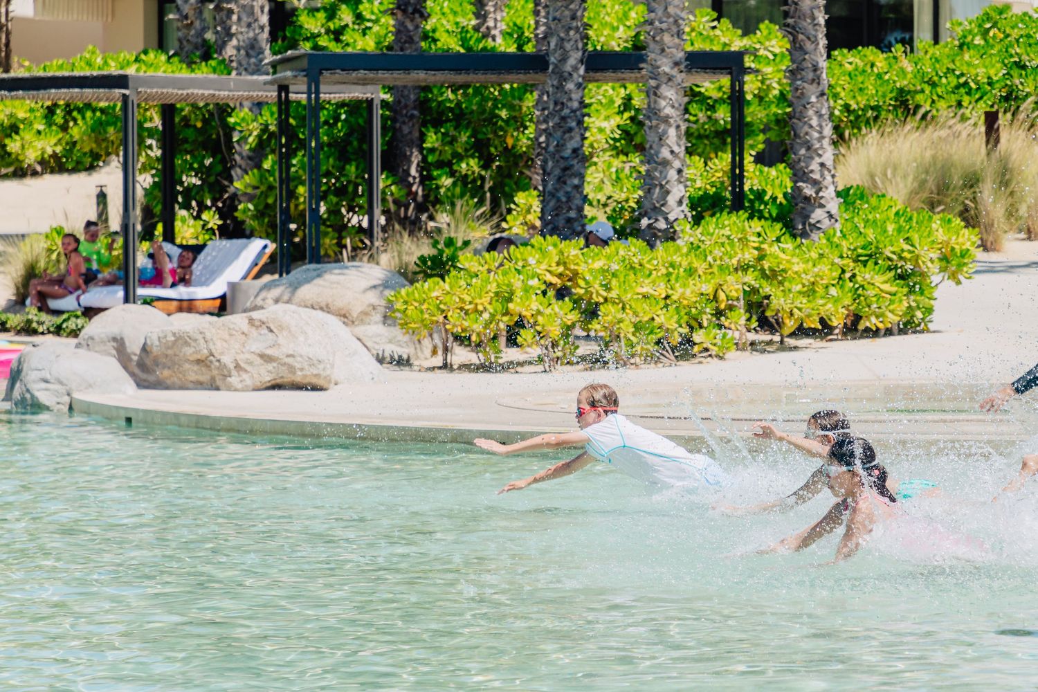 Beachgoers enjoy swimming and splashing in the crystal clear turquoise waters of a tropical beach resort.