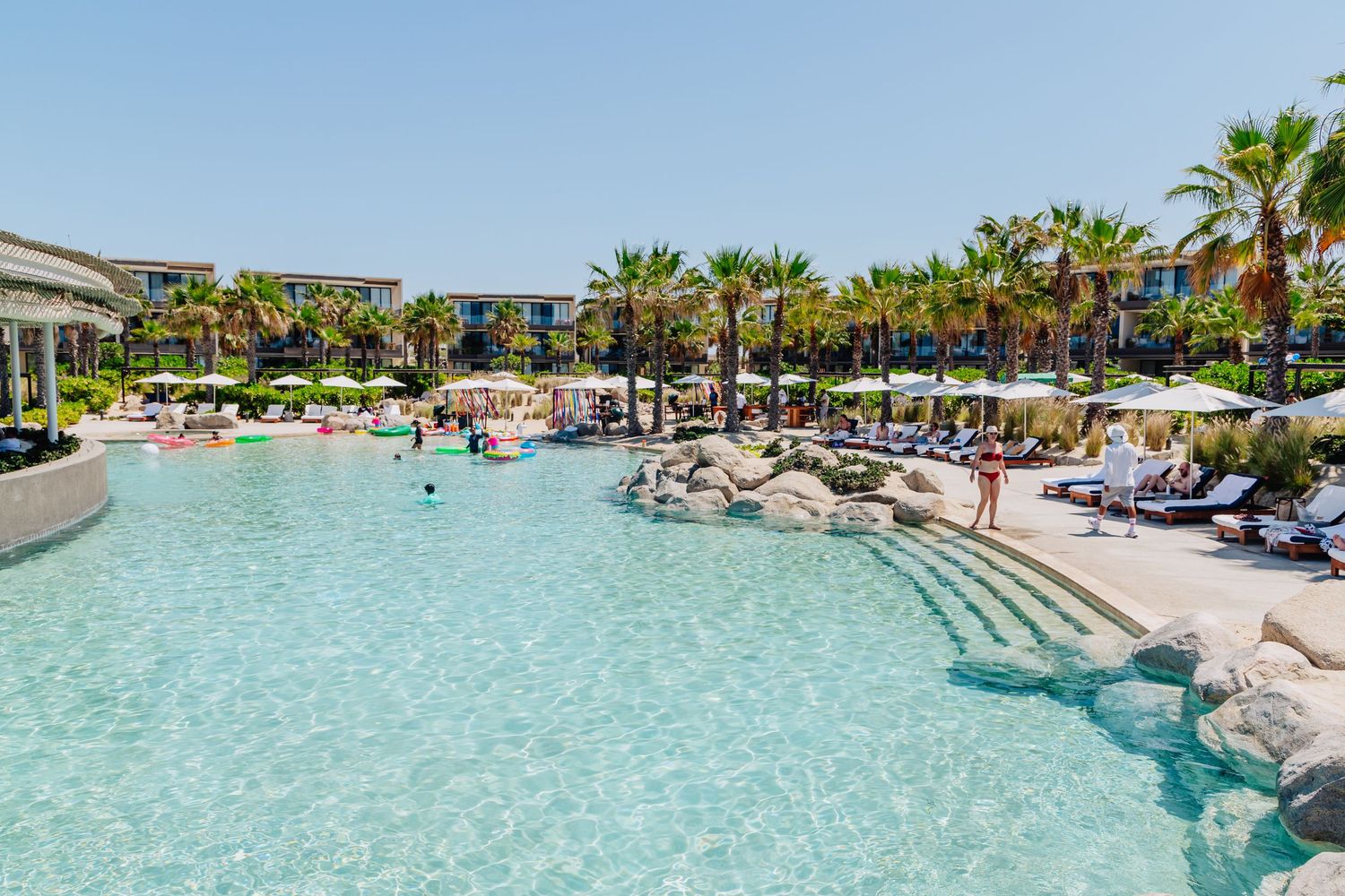 Luxurious resort swimming pool with palm trees, lounge chairs and clear turquoise water surrounded by tropical landscaping.