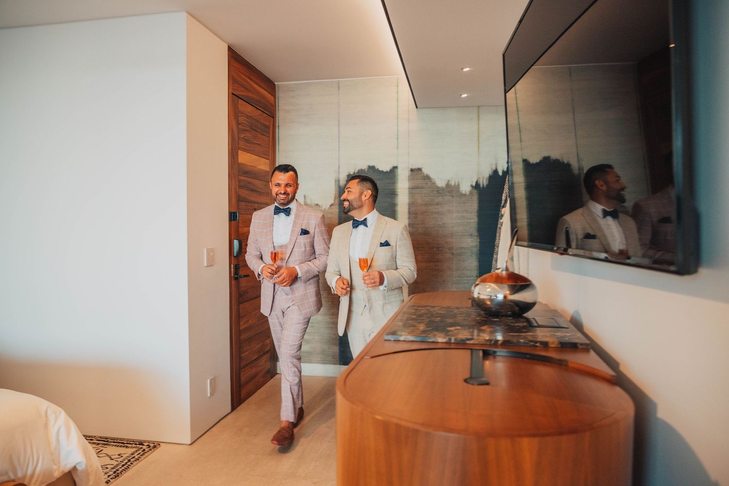 Two people in matching light suits walk through a modern interior hallway with drinks.
