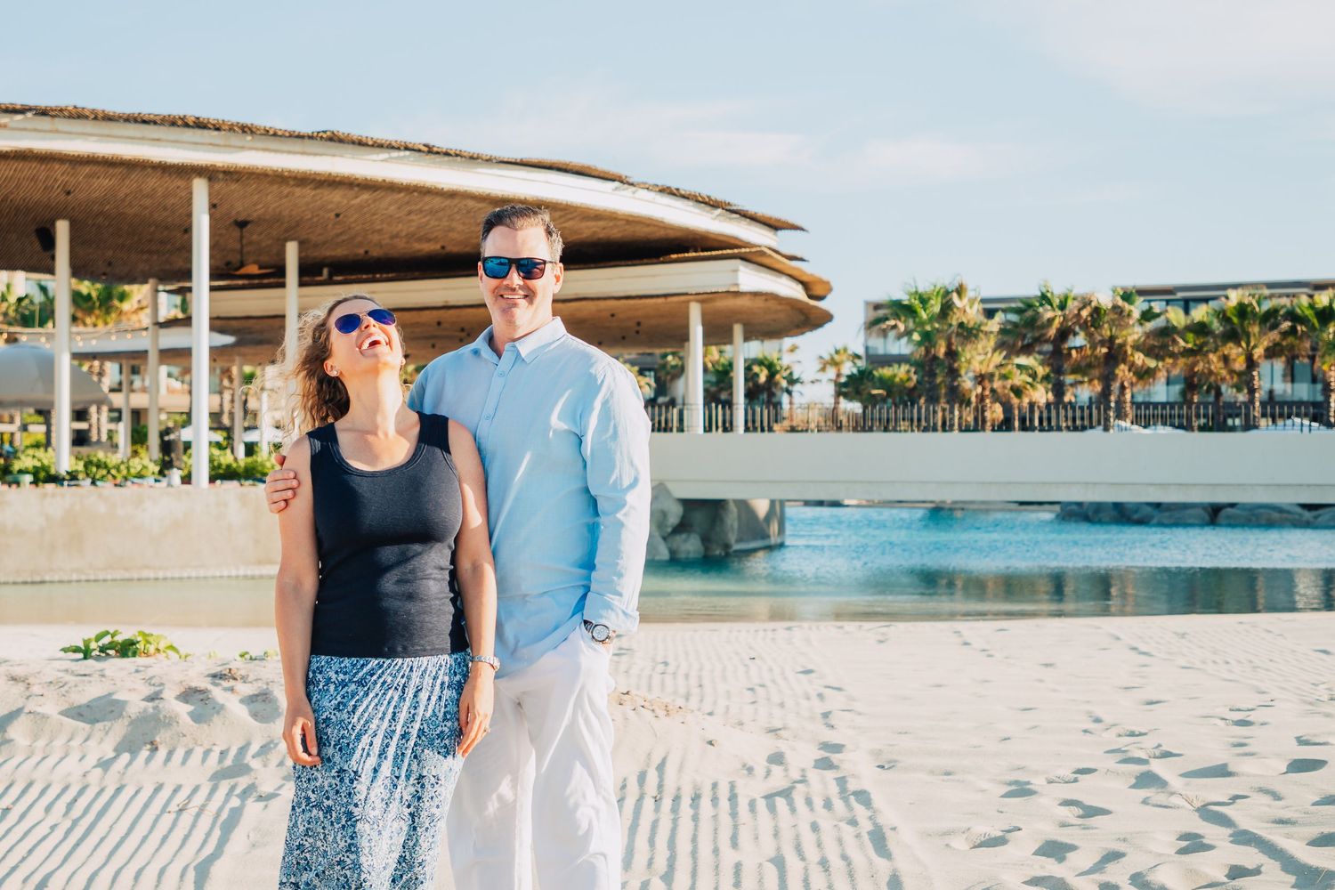 Couple enjoying a sunny day at a tropical resort with swimming pool and palm trees.