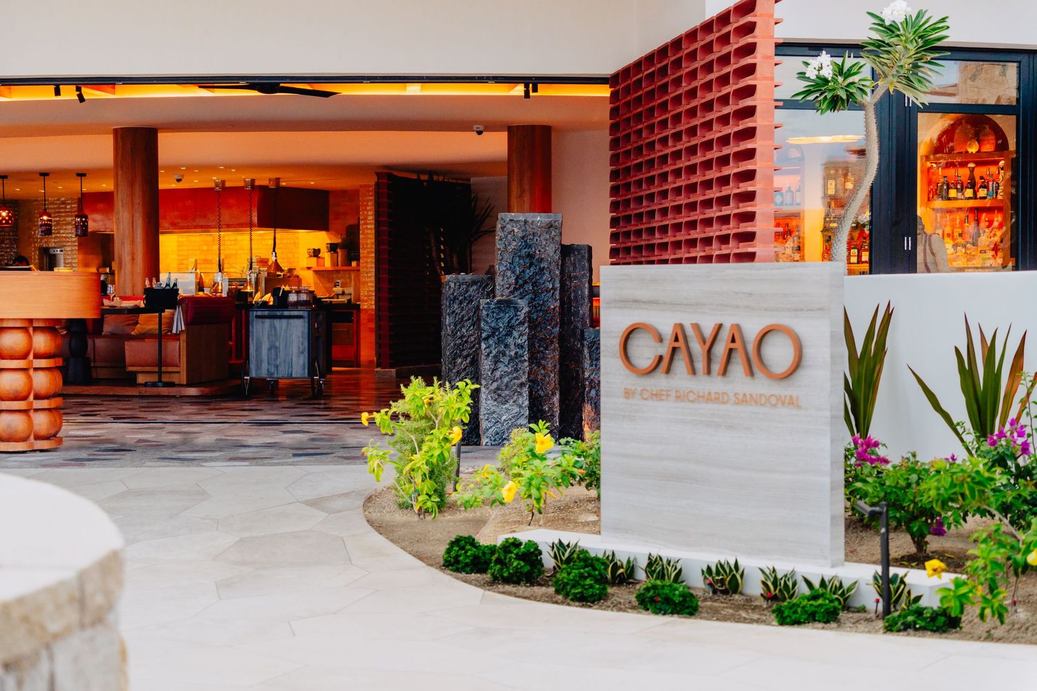 Modern resort entrance with red brick walls, warm lighting, and desert landscaping at dusk.