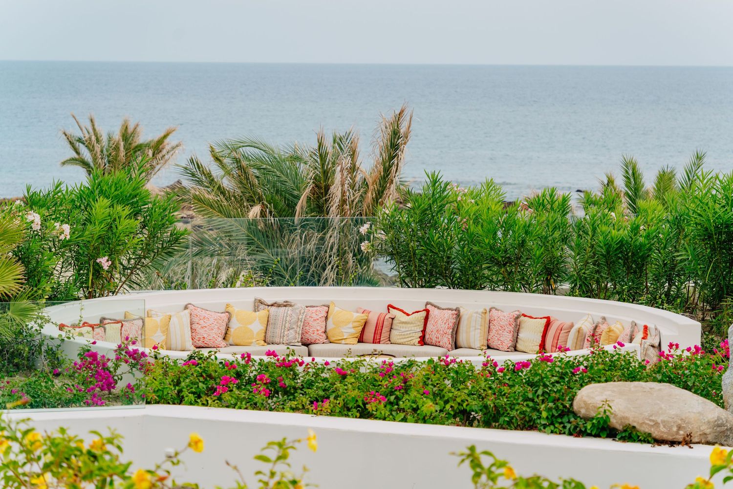 A curved stone wall with pink flowers and lush greenery against a misty coastal backdrop.