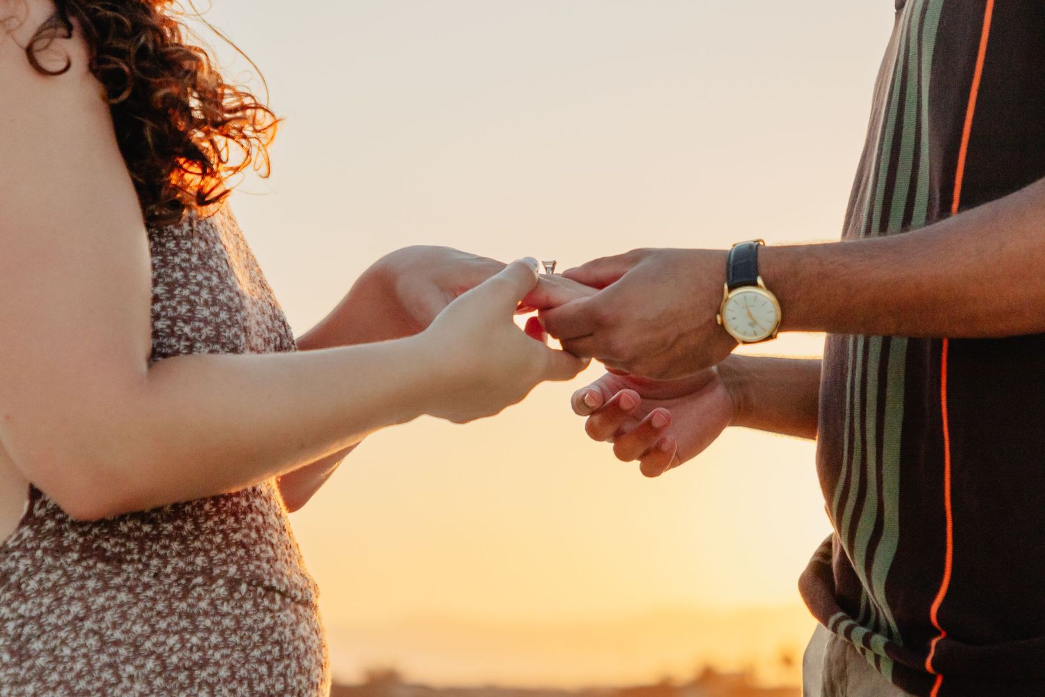 Hands exchanging rings during a sunset beach proposal.
