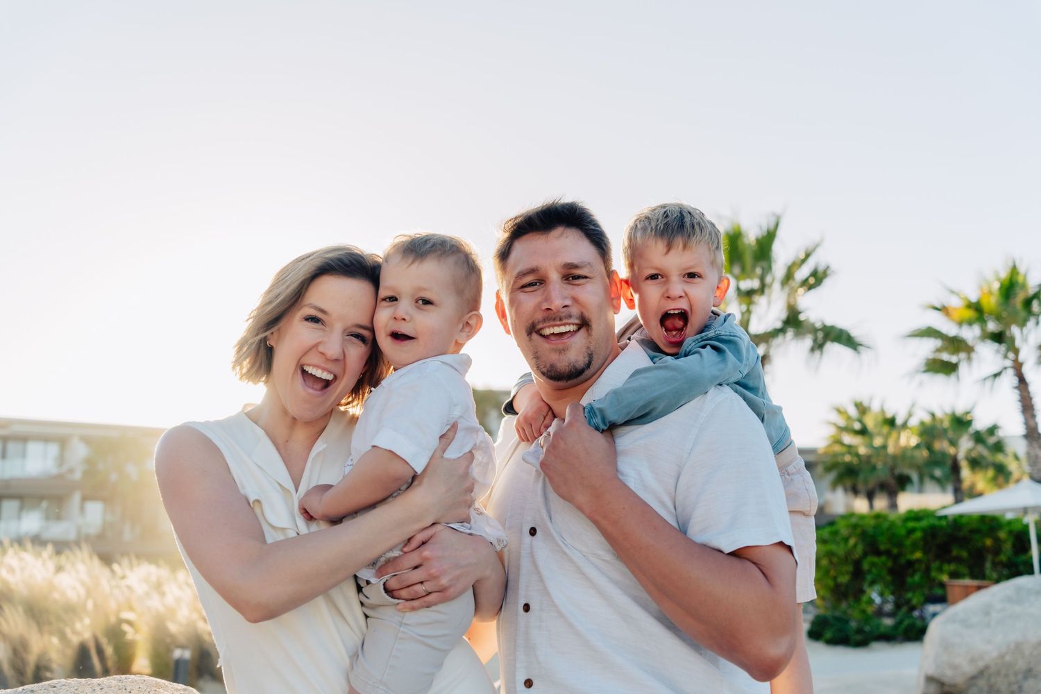 A happy family shares joyful moments together on a sunny beach with palm trees in the background.