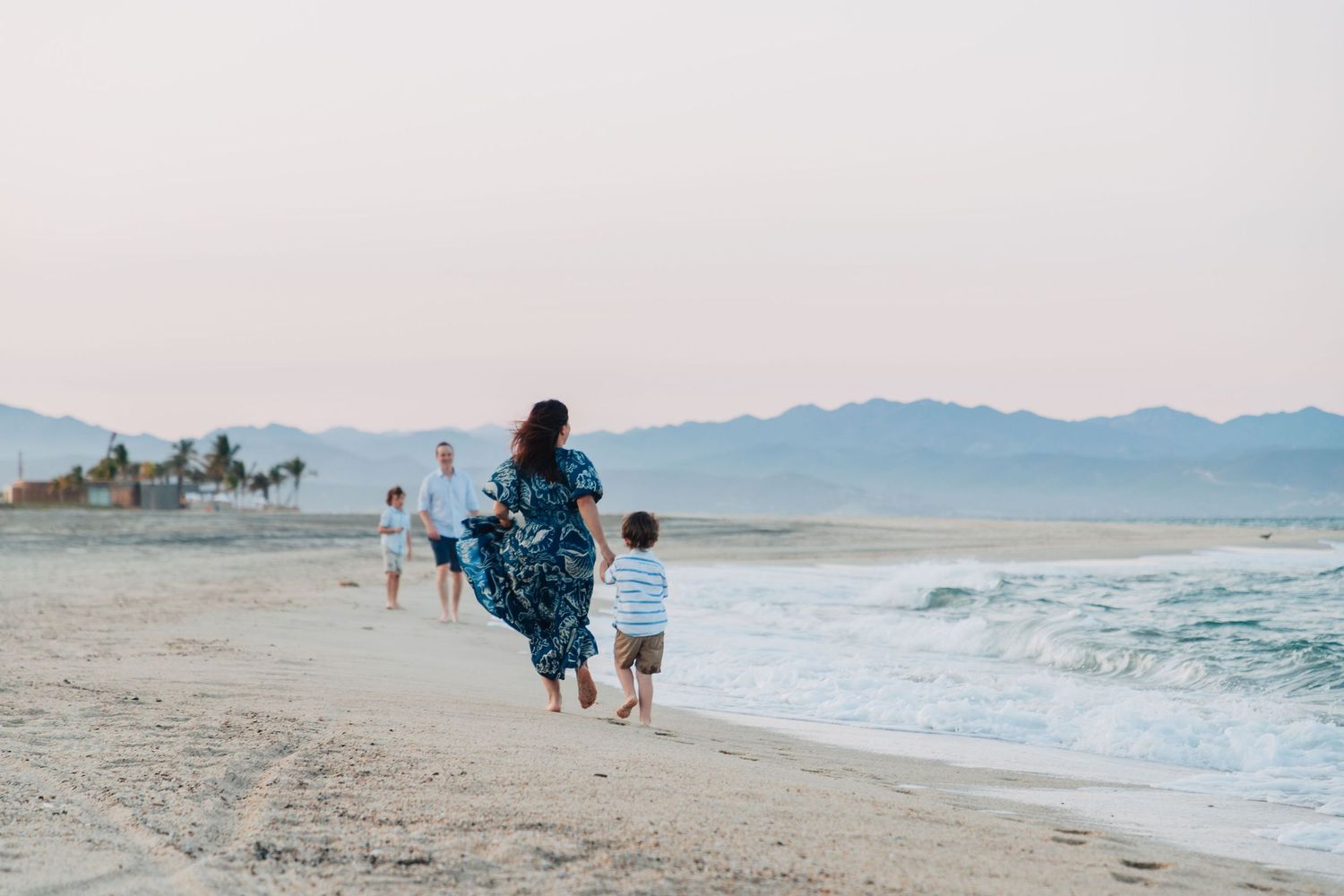 Scenic beach landscape at dusk with mountains in the distance and people walking along the shoreline.