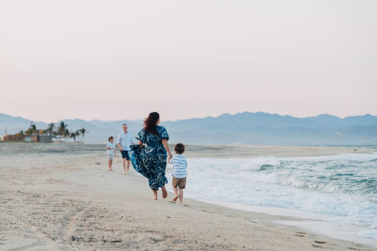 Sandy beach landscape with distant mountains and gentle ocean waves at dusk.