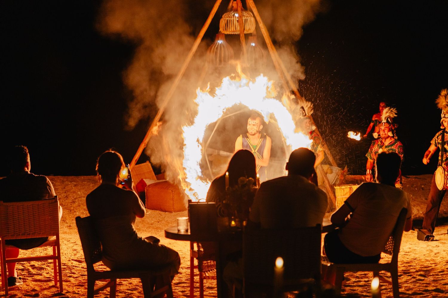 Dramatic fire dance performance illuminating the beach at night during an event.