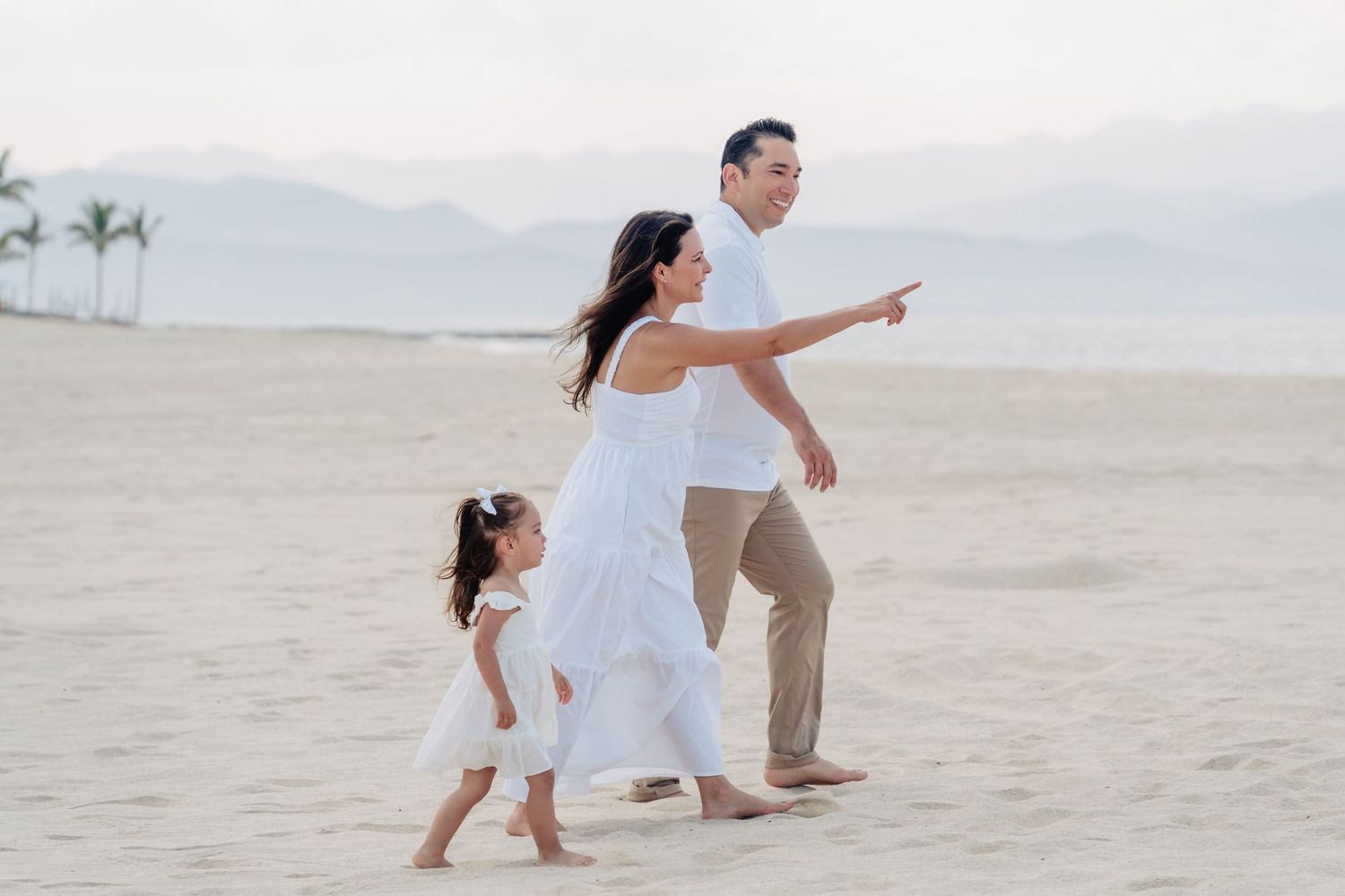 Family walking and pointing on sandy beach with mountains in background.