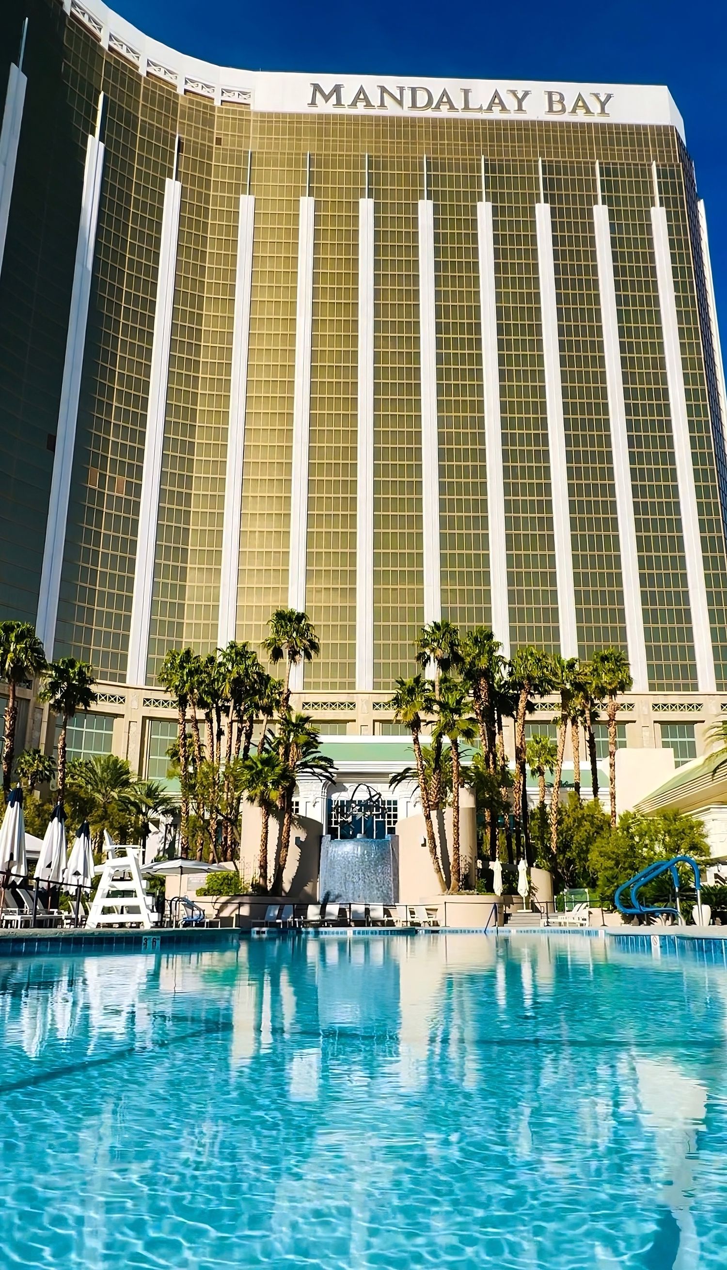 The luxurious Mandalay Bay hotel in Las Vegas with its sparkling blue pool and towering golden facade under clear skies.