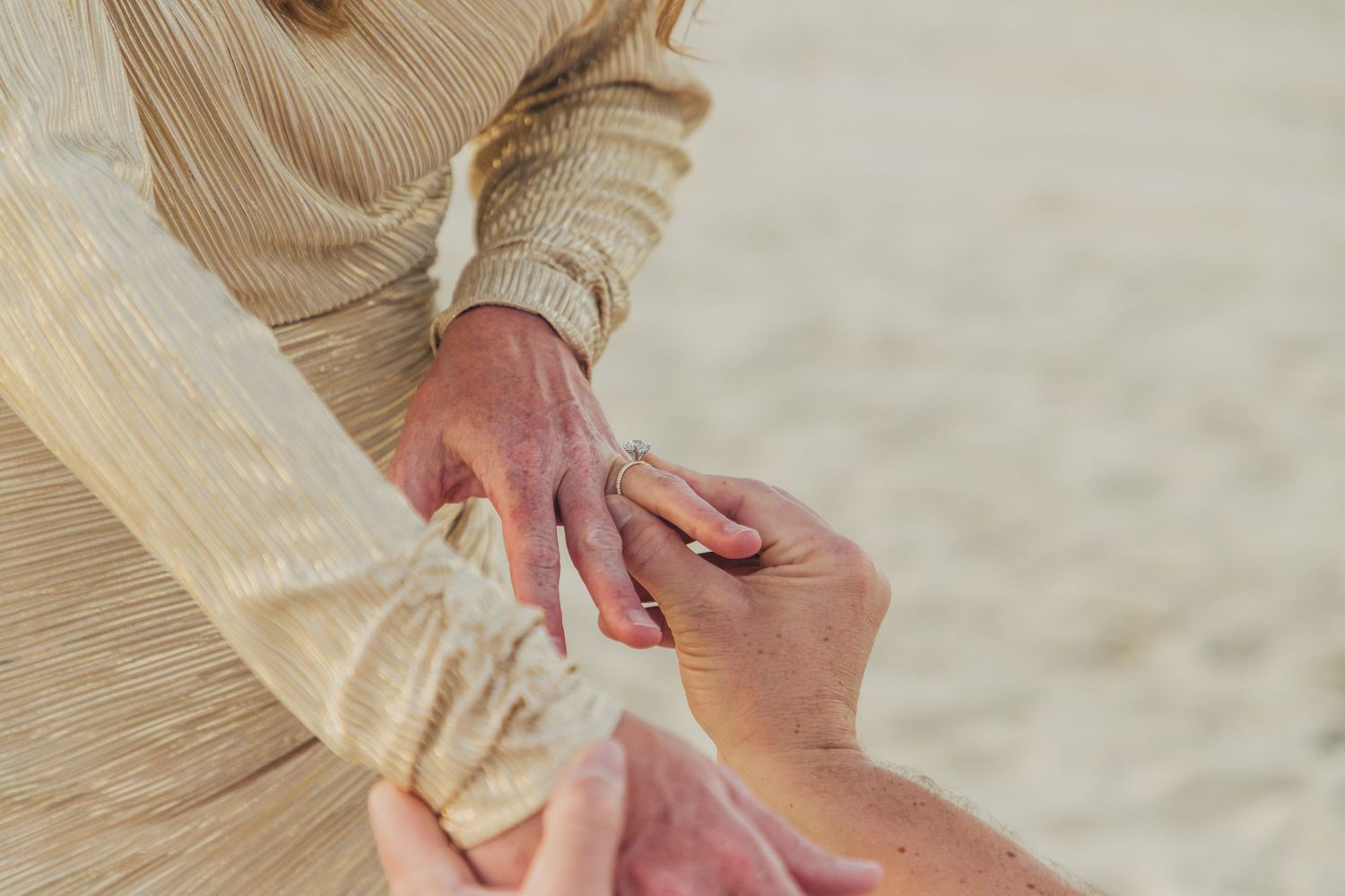 Close-up of hands presenting engagement ring during beach proposal.