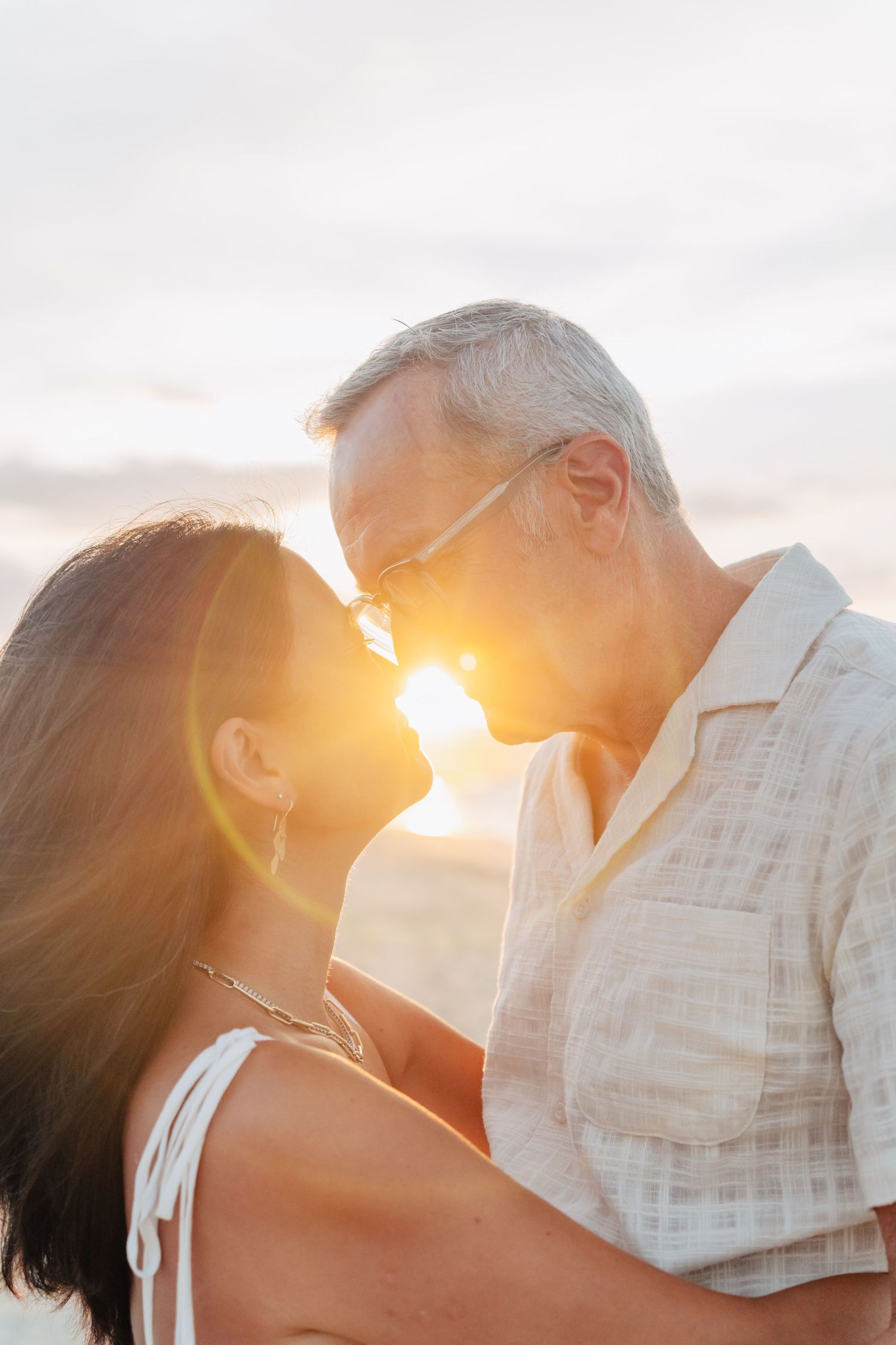 Silhouetted couple embracing at sunset with warm golden light creating a romantic backlit glow.