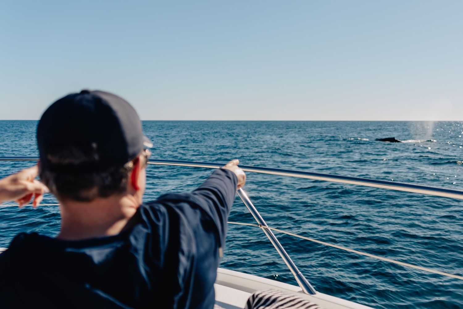 Boat cruising across blue ocean waters on a sunny day with waves trailing behind.