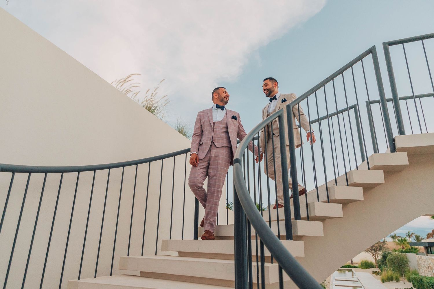 Two people in formal attire descending an elegant curved staircase with white railings.