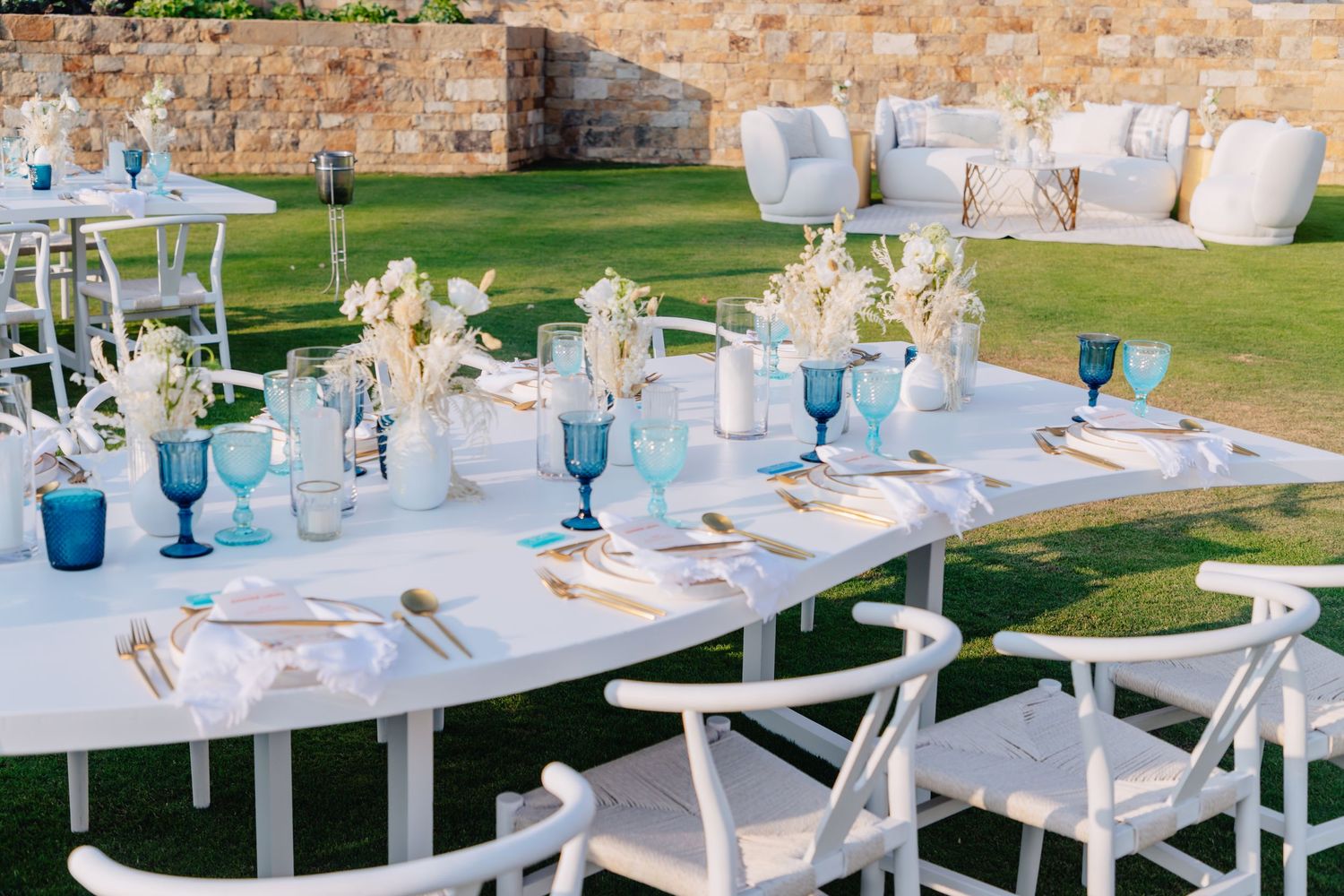 Elegant table settings with blue glassware and white linens at an outdoor reception.