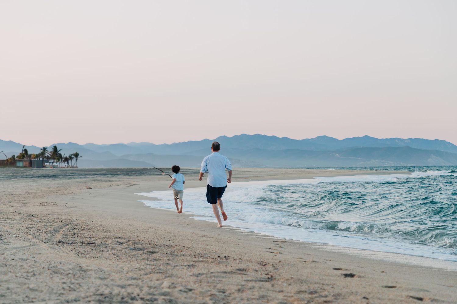 Serene beach scene with mountain backdrop and rolling waves at sunset.