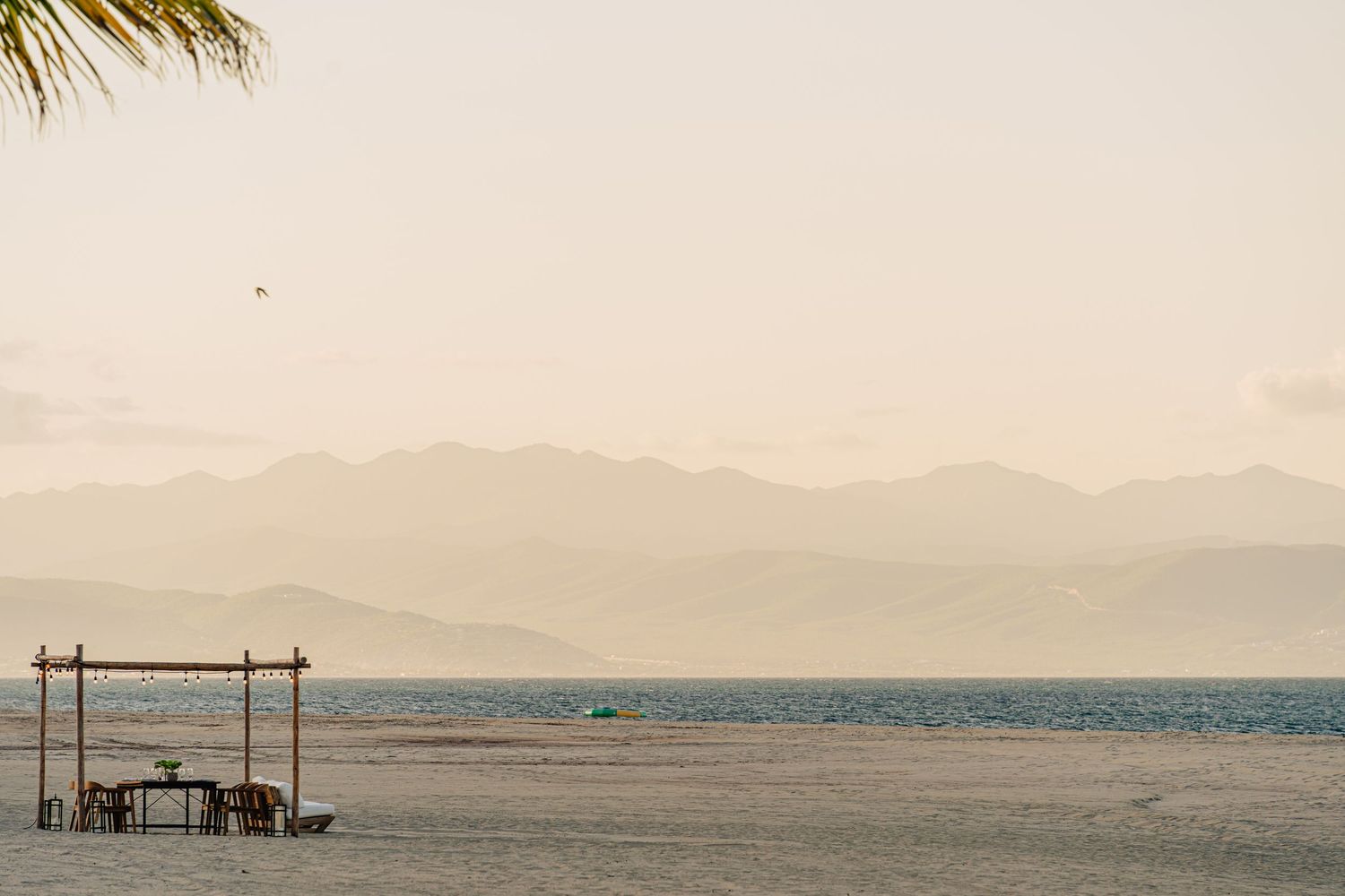A minimalist beach shelter stands on an empty shoreline with misty mountains in the distance under warm lighting.