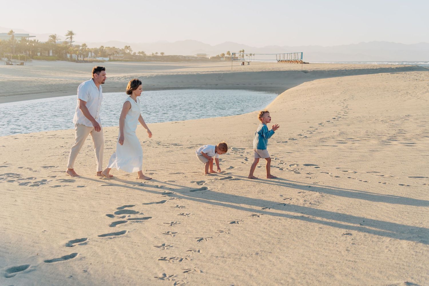 A family strolling along a sandy beach at sunset leaving footprints in their wake.