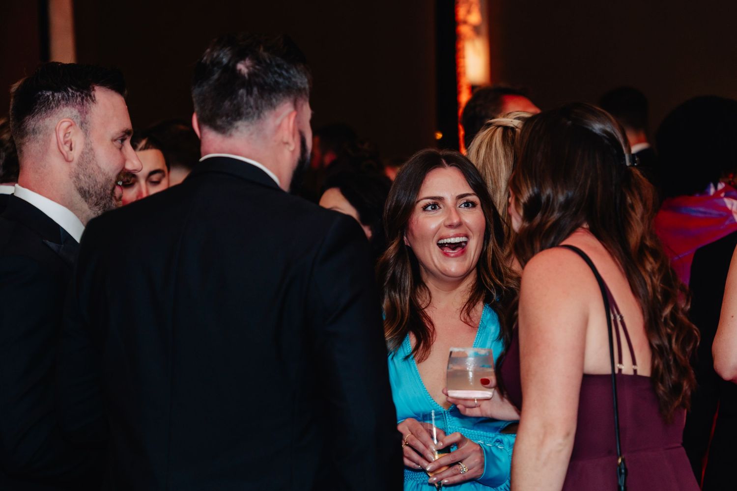 A group of people dancing and socializing at a dimly lit evening party or reception.
