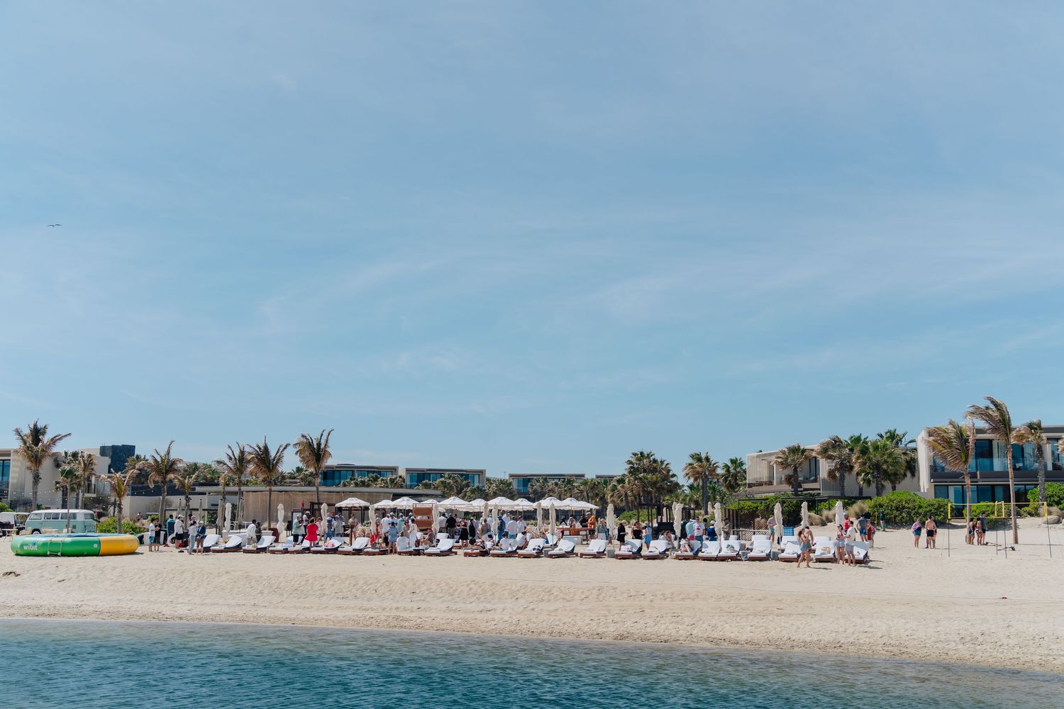 Beach resort with lounge chairs and umbrellas lined up along the shoreline under blue skies.