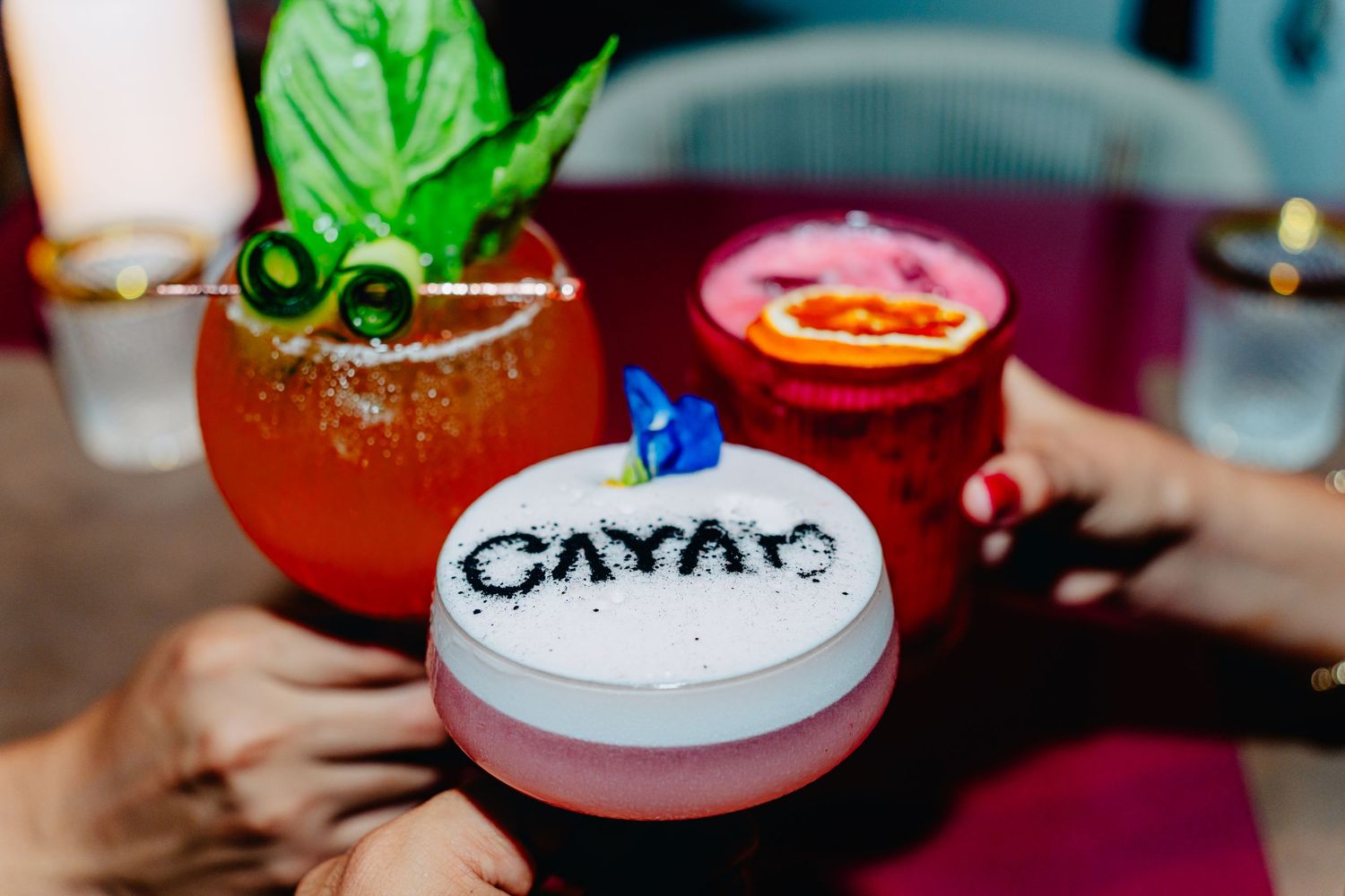 Colorful cocktails garnished with fresh herbs and decorative foam art at an upscale bar.