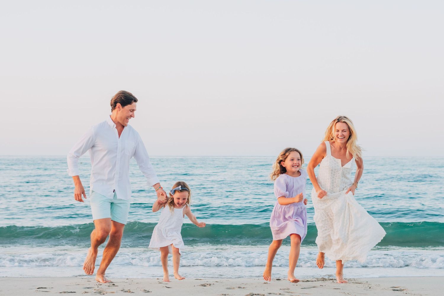 Family playing and running together along a sunny beach with ocean waves in the background.