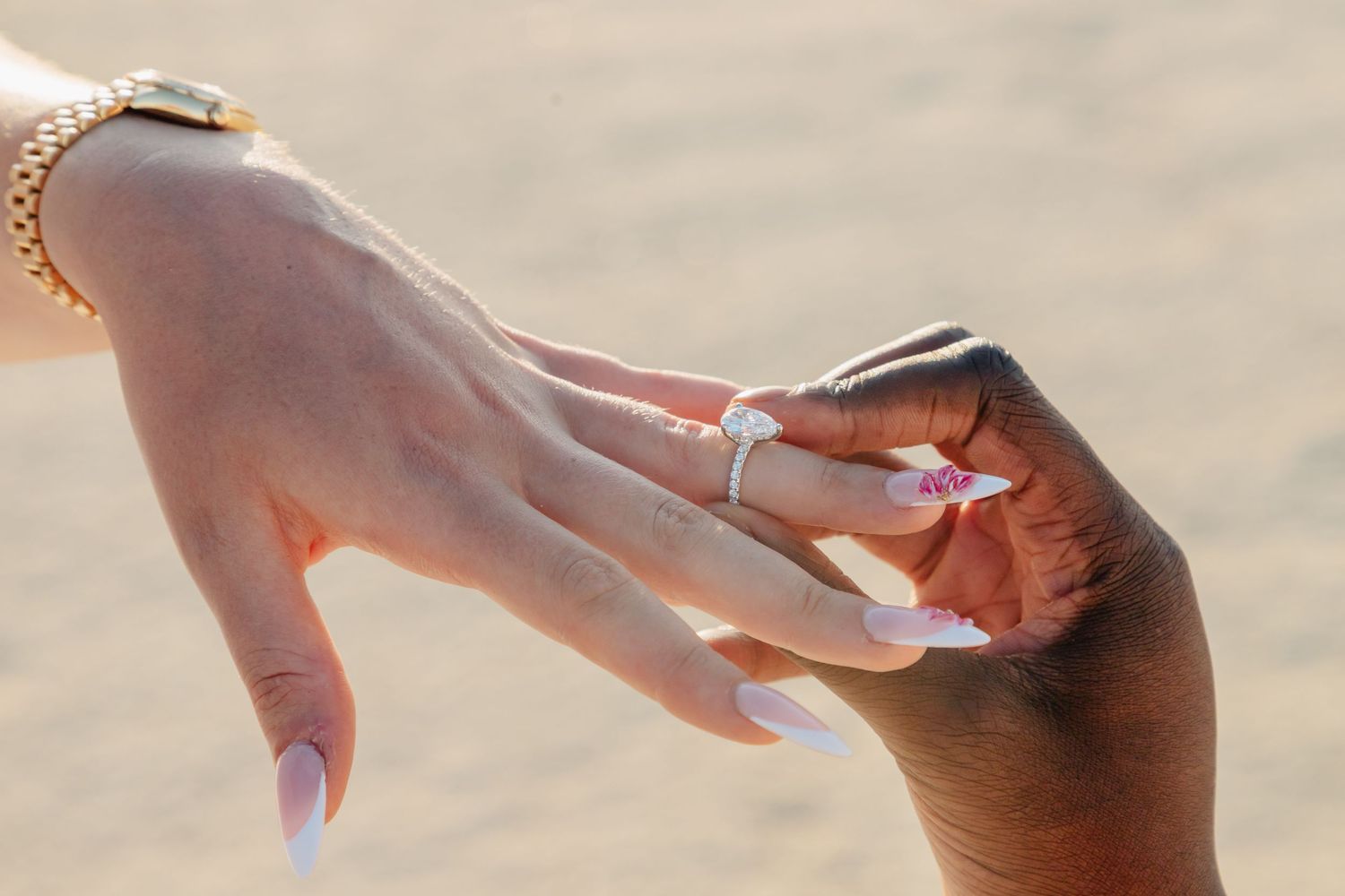 Close-up of hands exchanging rings on a sandy beach during sunset.