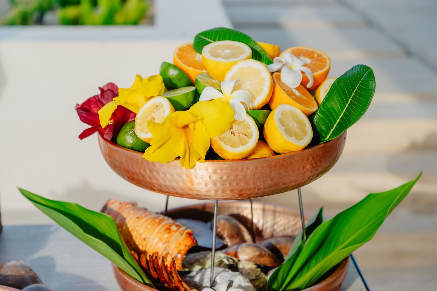 Fresh tropical fruits and vegetables arranged in a copper serving bowl with decorative leaves and garnishes.
