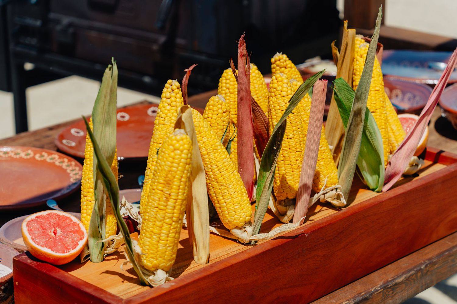 Fresh corn on the cob arranged in a wooden serving tray with citrus garnish.