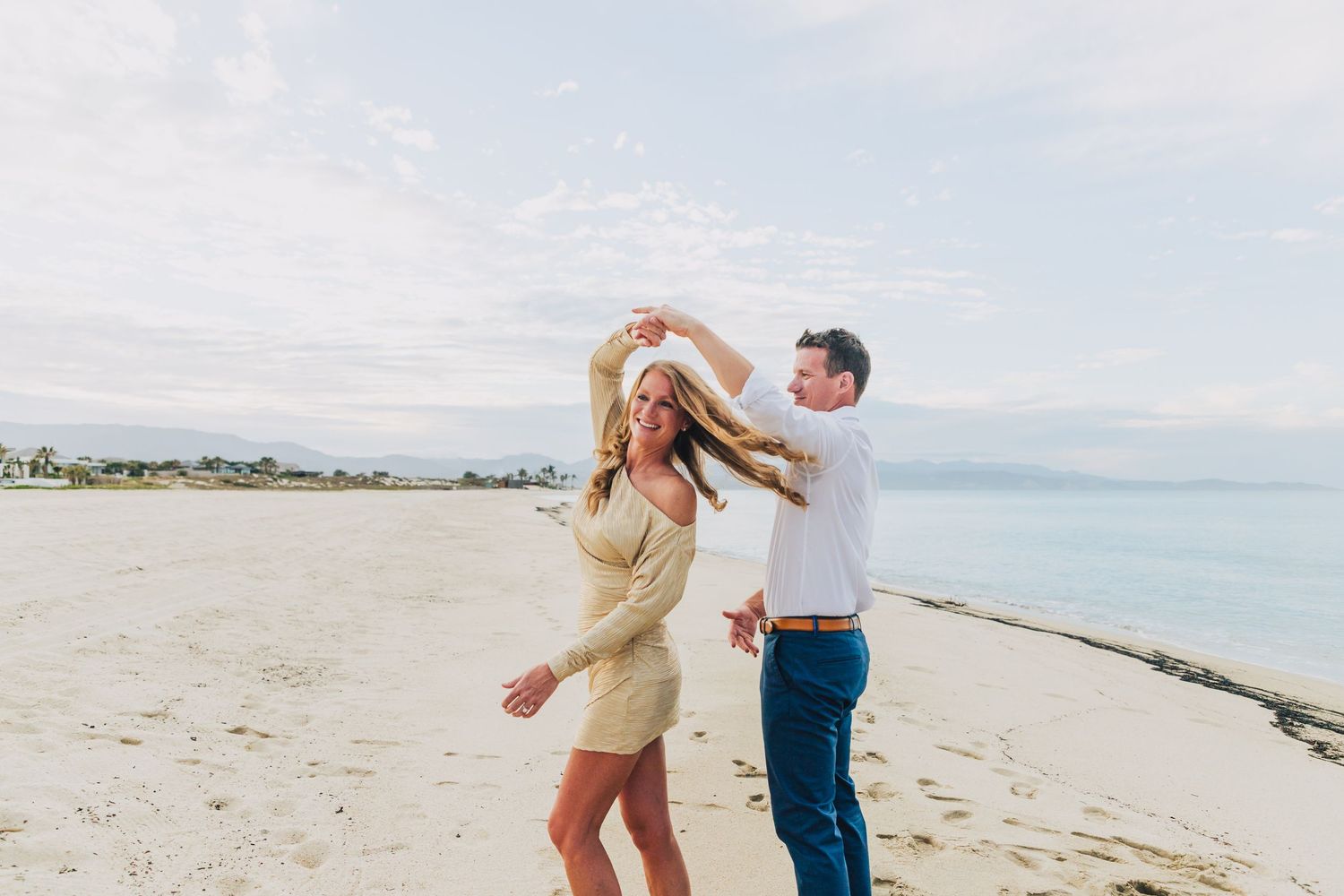A couple walks along a serene beach shoreline during a bright sunny day.