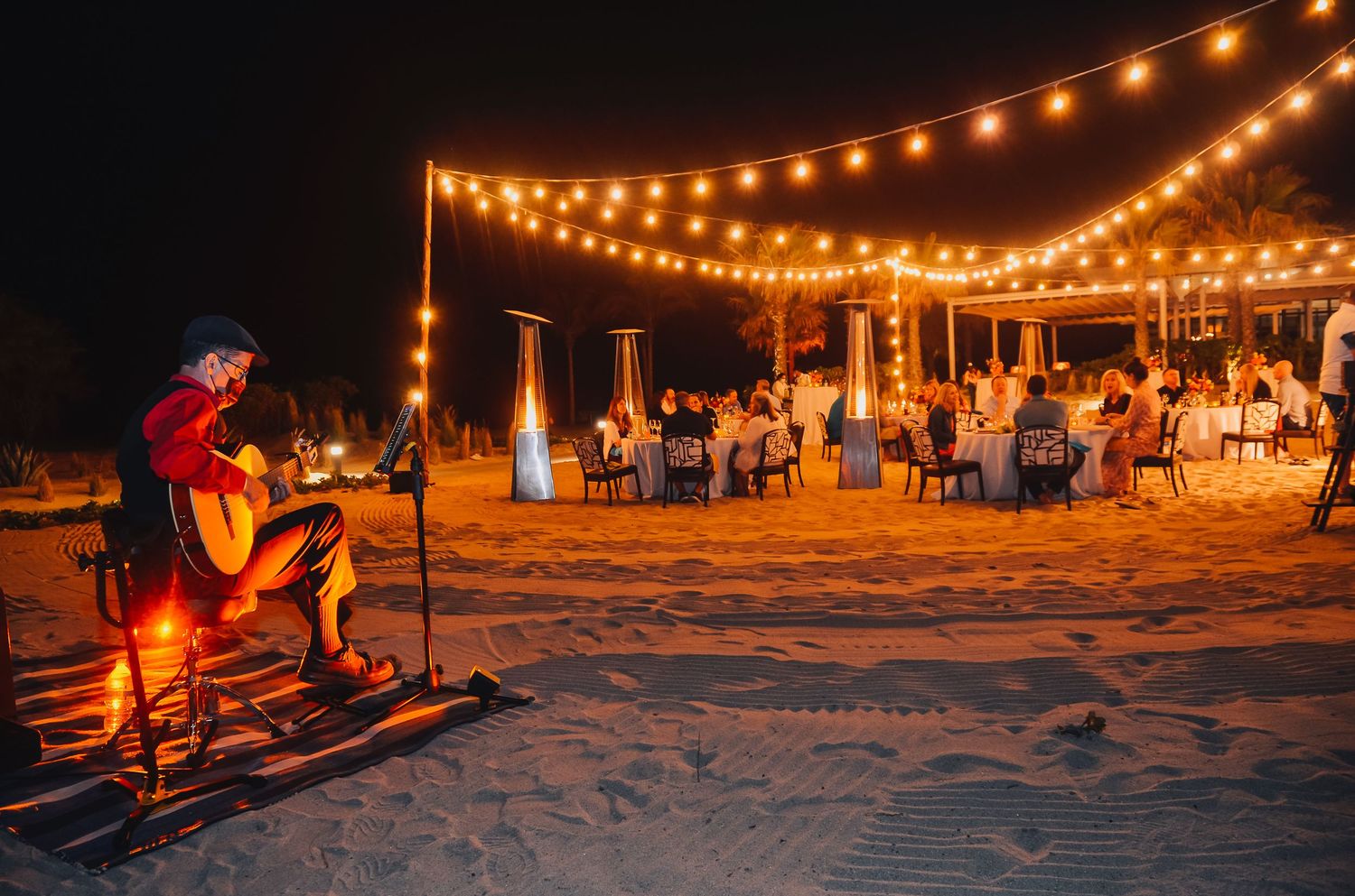 Beach reception at night with string lights and live acoustic entertainment.